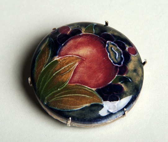 alt="small circular ceramic brooch red pomegranate on dark blue background"
