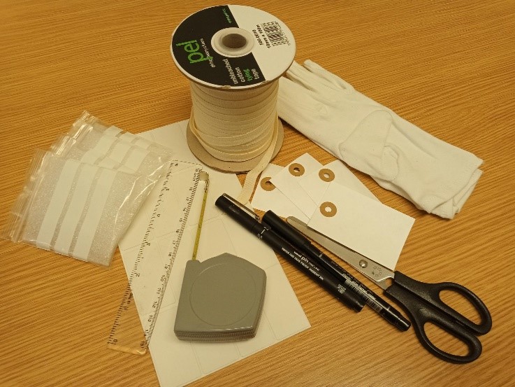 an assortment of items used while accessioning, a table top showing string, white gloves, pens, scissors, a ruler, blank labels
