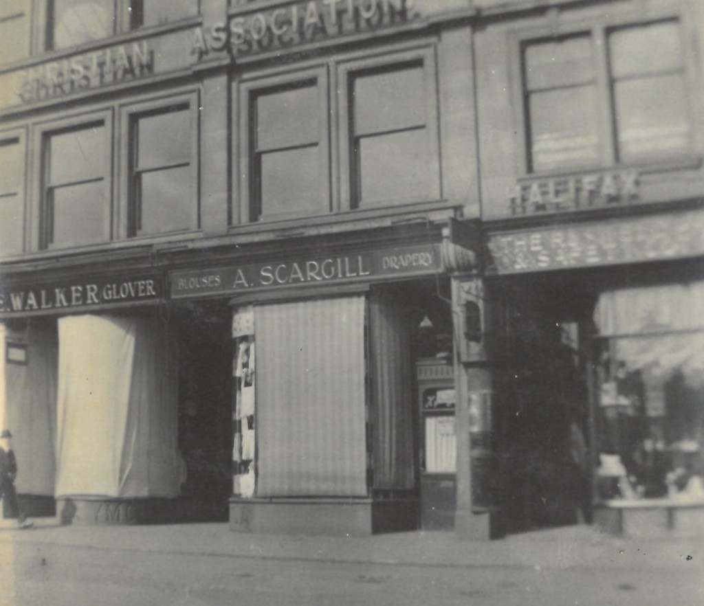 Photograph showing the detail of the shopfronts on the ground floor. The shop signs say Walker (Glover) A Scargill (Blouses and Drapery). A  Halifax sign is visible on the next door building.
