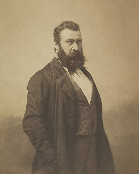 A photograph of Millet who has a bushy beard and is wearing a long coat