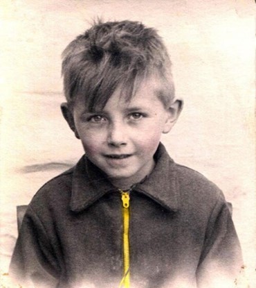 Brian as a child, wearing a zip up jacket with a yellow zip